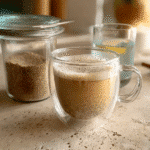 Frothy bariatric seed trick drink served in a glass cup with lemon water and seed jar in background