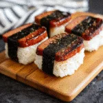 Spam musubi recipe with glazed Spam and seaweed wrapped over white rice on wooden board