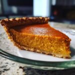 A close-up of a perfect slice of Amazing Pumpkin Pie on a plate, showcasing its rich orange filling and flaky crust.