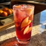 A tall glass filled with red Apple Cider Sangria, ice, and slices of apple and berries.