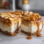 A delicious Caramel Apple Cheesecake with a slice cut out, showing the creamy filling and apple topping.