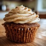 A close-up of a delicious Chai Spiced Cupcake topped with swirl of creamy frosting and a dusting of cinnamon.