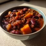 A close-up of a bowl of chili with pumpkin, kidney beans, and ground meat.
