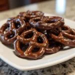 A pile of delicious chocolate dipped pretzels on a white plate, ready to be enjoyed.