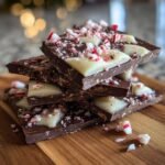 A close-up stack of dark chocolate peppermint bark pieces, topped with white chocolate swirls and crushed candy canes.