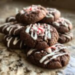 A stack of rich chocolate peppermint cookies drizzled with white icing and topped with crushed candy canes.