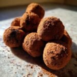 A close-up of a pile of rich, dark chocolate truffles generously coated in cocoa powder.