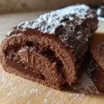 A close-up of a rich chocolate Yule Log Cake, dusted with powdered sugar and drizzled with chocolate ganache.