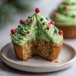 A delicious Christmas Tree Cupcake with green frosting and festive sprinkles, with a bite taken out.