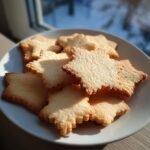 A pile of golden-brown Classic Sugar Cookies shaped like stars on a white plate, with a blurred background.