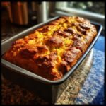 A golden-brown loaf of freshly baked cornbread stuffing in a loaf pan, ready to be used.