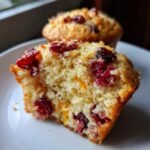 Close-up of a halved Cranberry Orange Muffin, showing juicy cranberries and orange zest within the fluffy crumb.
