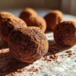 Close-up of several easy chocolate truffles generously coated in cocoa powder, with some scattered on a marble surface.
