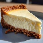 A close-up of a creamy slice of Eggnog Cheesecake with a graham cracker crust on a grey plate.