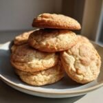 A stack of chewy Eggnog Cookies dusted with cinnamon sugar on a grey plate, bathed in warm sunlight.