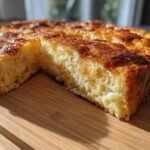 A golden brown slice of Eggnog French Toast Bake on a wooden cutting board, showing its fluffy interior.