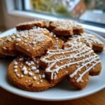 A close-up of a plate of freshly baked gingerbread cookies, decorated with white icing and sugar sprinkles.