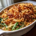 Close-up of a classic Green Bean Casserole in a white baking dish, topped with golden fried onions.