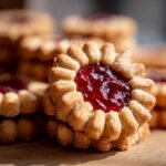 Close-up of a classic Linzer cookie filled with glistening raspberry jam, showcasing its intricate edges and sugar dusting.