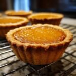 Close-up of a golden-brown mini pumpkin pie with a flaky crust, cooling on a wire rack.