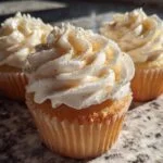 Three New Year’s Eve Champagne Cupcakes topped with white frosting and gold edible glitter.