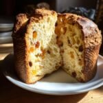 A close-up of a sliced Panettone bread, showing its fluffy interior with raisins and candied fruit.