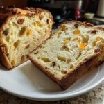 Close-up of sliced Panettone on a white plate, showing its fluffy interior with raisins and candied orange peel.