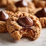 A close-up of a Peanut Butter Blossoms cookie with a bite taken out, showing the gooey chocolate center.