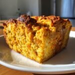 A close-up of a moist and golden slice of Pumpkin Bread Pudding on a white plate.