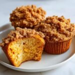 Close-up of three Pumpkin Muffins with Streusel, one is bitten into, revealing a fluffy interior.