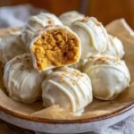 A pile of white chocolate-covered Pumpkin Spice Truffles, with one truffle cut in half to reveal the moist, spiced interior.
