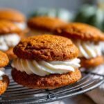 Close-up of a delicious Pumpkin Whoopie Pie with fluffy white cream filling on a cooling rack.