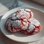 Three delicious Red Velvet Crinkle Cookies dusted with powdered sugar on a light pink plate.