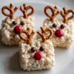 Close-up of three Reindeer Rice Krispie Treats decorated with pretzels for antlers, chocolate balls for eyes, and red candies for noses.