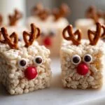 Close-up of a Reindeer Rice Krispie Treat with pretzel antlers, candy eyes, and a red candy nose.