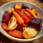 A close-up shot of a bowl filled with colorful roasted root vegetables, including carrots, beets, and onions.