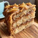 A generous slice of Salted Caramel Apple Cake, featuring layers of moist cake and rich caramel filling, topped with swirls of caramel frosting.