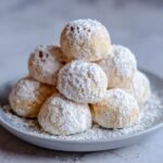 A close-up of a pile of delicious Snowball Cookies dusted generously with powdered sugar.