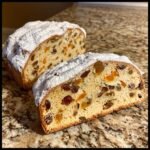 Close-up of two slices of Stollen, a festive bread, generously filled with raisins and dried apricots, dusted with powdered sugar.