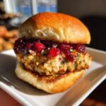 Close-up of a delicious Turkey and Cranberry Slider on a white plate, topped with cranberry sauce and herbs.