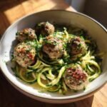 A bowl of Garlic Butter Meatballs served over zucchini noodles, garnished with fresh parsley.