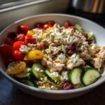 A close-up of a vibrant Greek Chicken Quinoa Bowl filled with quinoa, chicken, cherry tomatoes, cucumber slices, olives, and feta cheese.