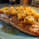A close-up of a perfectly grilled salmon fillet topped with caramelized pineapple chunks.