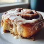 Close-up of a soft, fluffy homemade cinnamon roll generously topped with white icing.