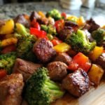 A close-up shot of a Keto Steak and Veggies Sheet Pan Dinner featuring browned steak bites, broccoli florets, and colorful bell peppers on a wooden board.