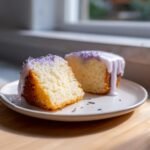 Two slices of moist lavender cake with a light purple glaze and lavender sprinkles on a white plate.