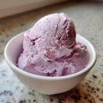 Close-up of three scoops of creamy purple lavender ice cream in a white bowl.