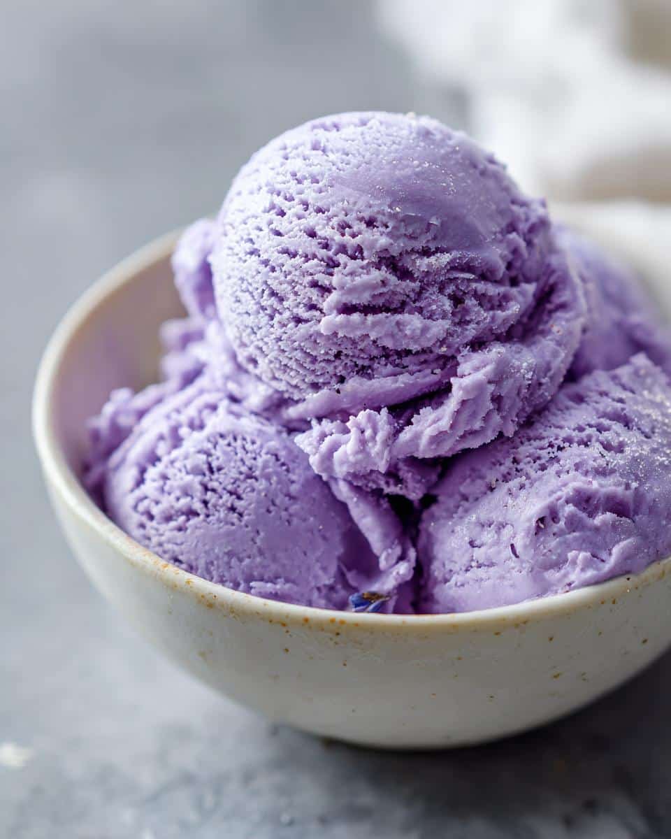 Divine lavender ice cream: 1 magical recipe 9 Close-up of creamy scoops of purple lavender ice cream in a bowl, with a hint of lavender buds visible.