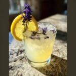 A refreshing glass of lavender lemonade with ice, garnished with a lemon slice and fresh lavender sprigs.