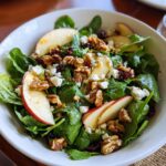 A vibrant Apple Arugula Salad with sliced apples, walnuts, cranberries, and feta cheese in a white bowl.